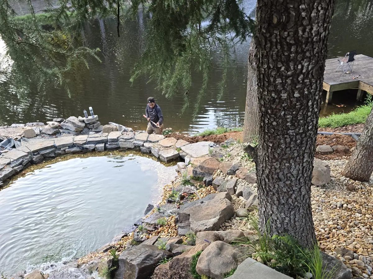 A Georgia Pond & Waterfall crew member setting stone around a lakeside pond build