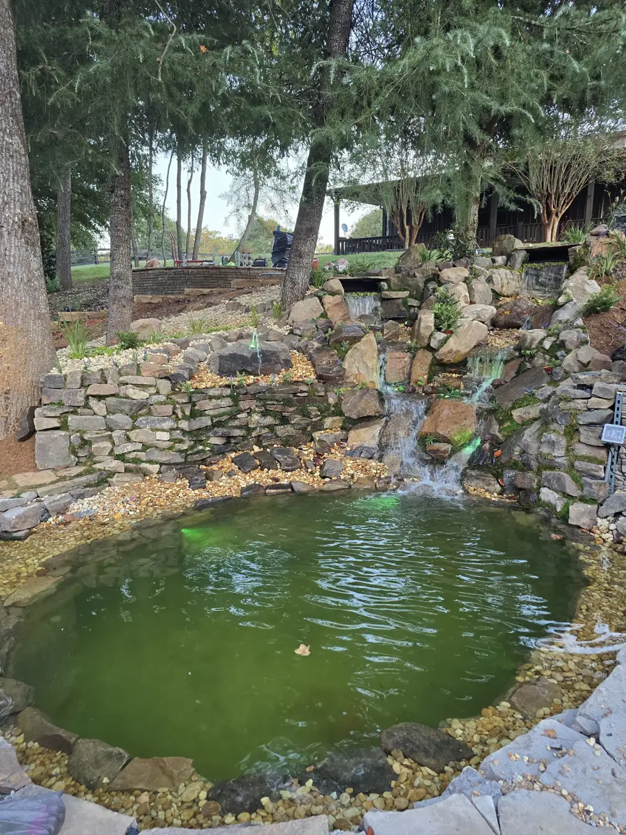 Multi-tier boulder waterfall with underwater lighting spilling into a pebble-lined pond